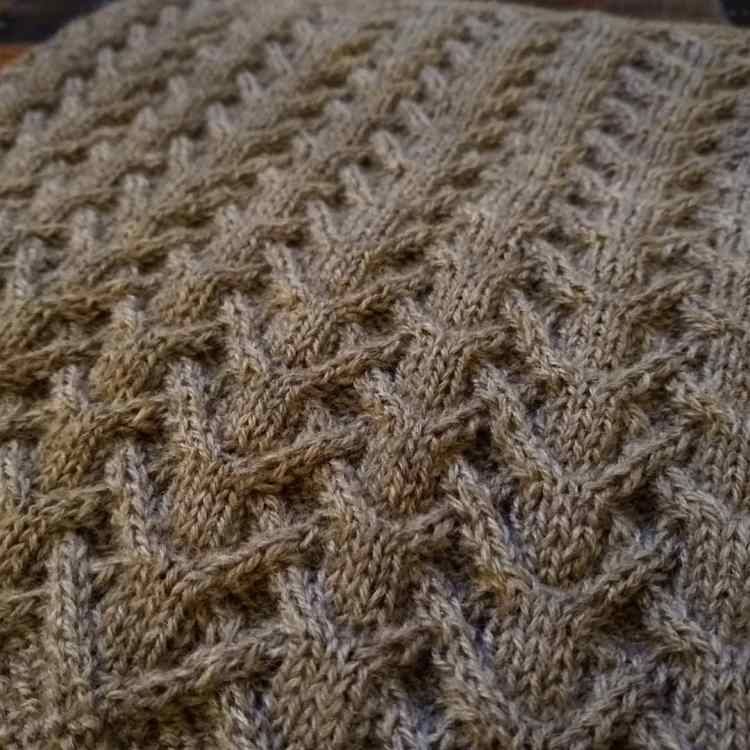A close-up of the interlacing cables on a cowl knit in a soft, warm gray yarn.
